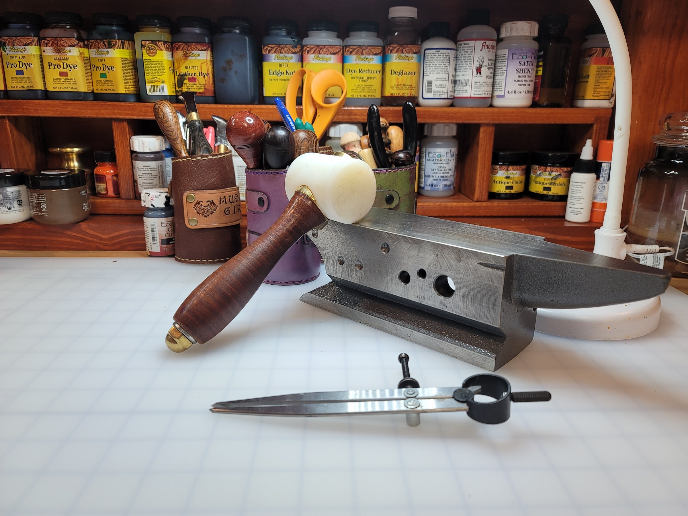 A leatherworking bench with a mallet, anvil, tools and shelves of leather dye